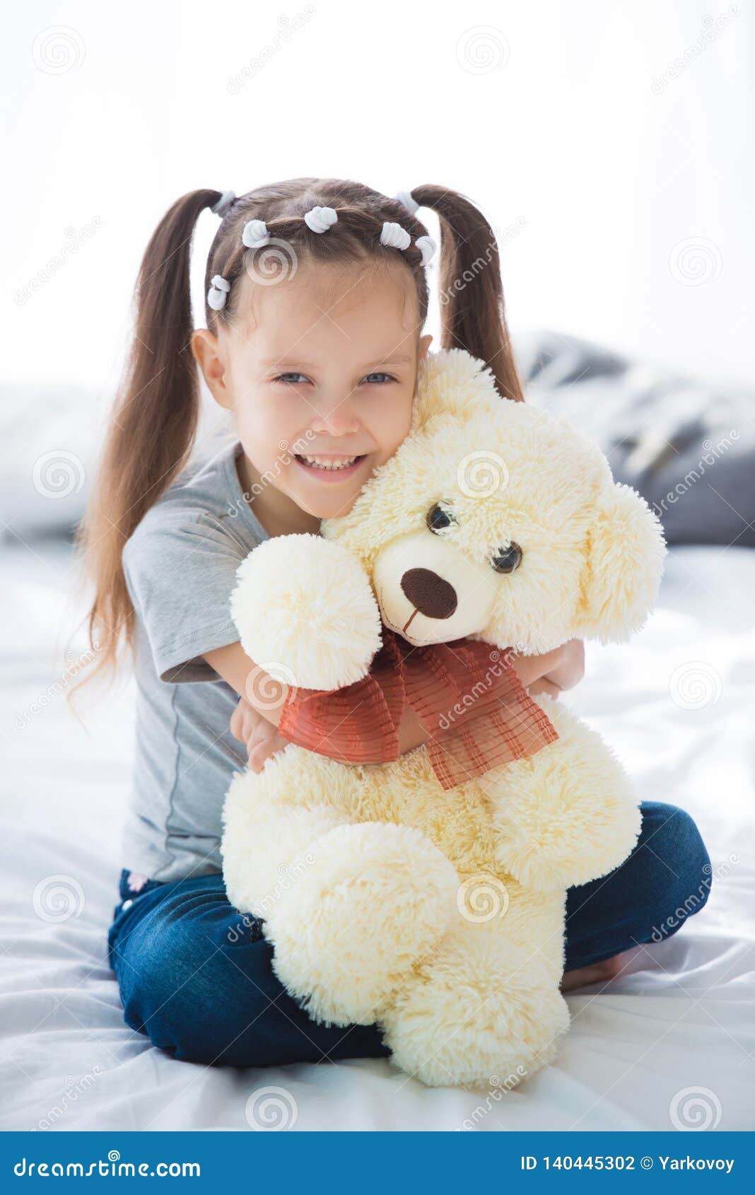 Adorable Smiling Littlegirl Sitting on a Bed Hugging a White Teddy Bear ...