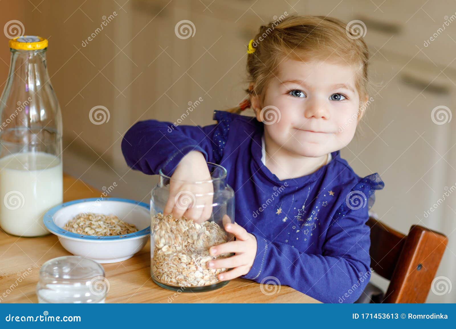 adorable toddler girl eating healthy oatmeals with milk for breakfast. cute happy baby child in colorful clothes sitting