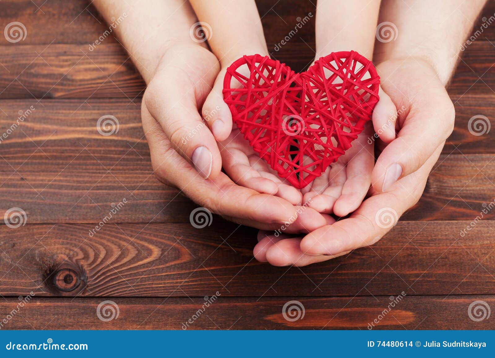 adult and child holding red heart in hands over a wooden table. family relationships, health care, pediatric cardiology concept.