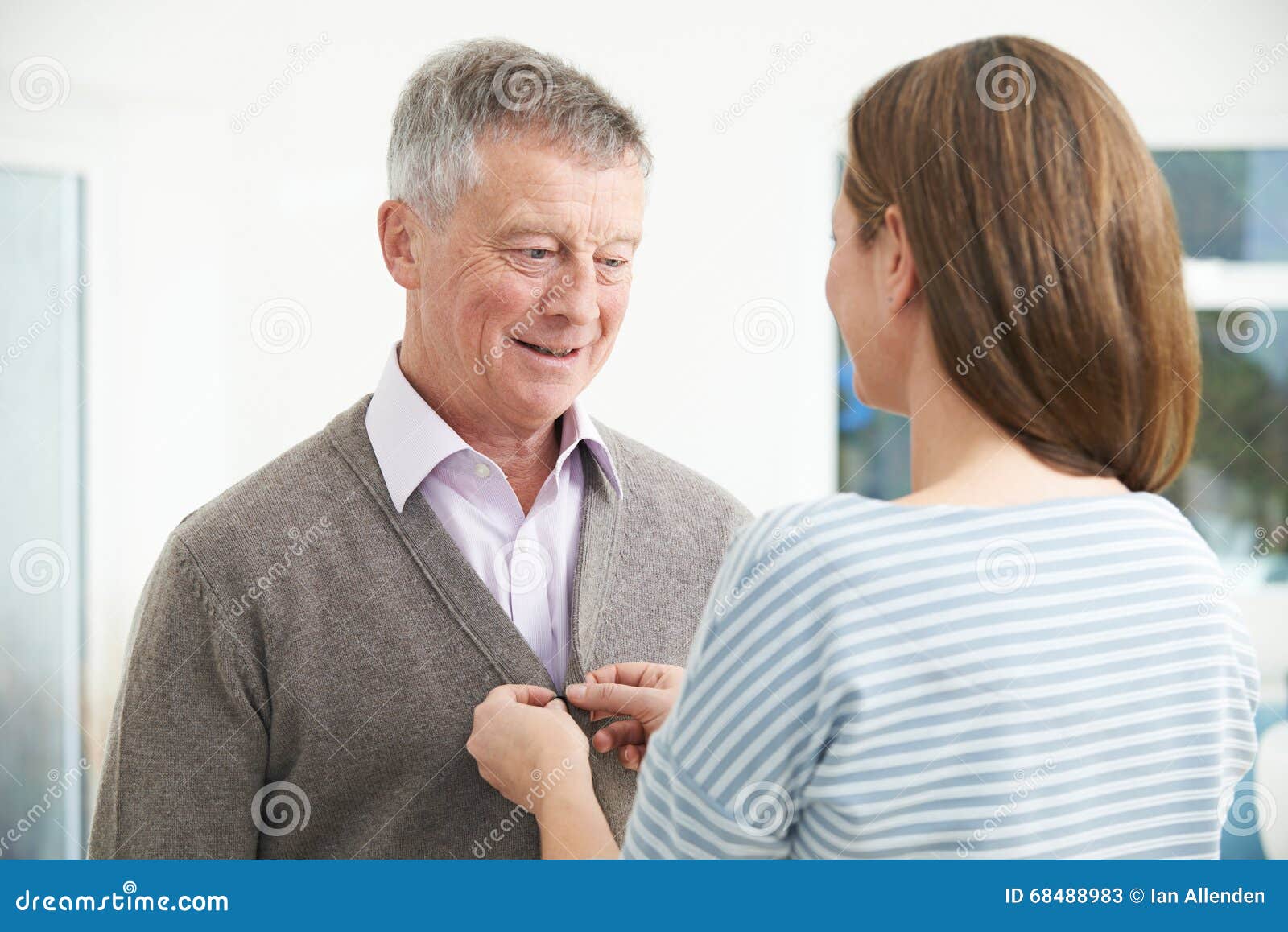 adult daughter helping senior man to button cardigan
