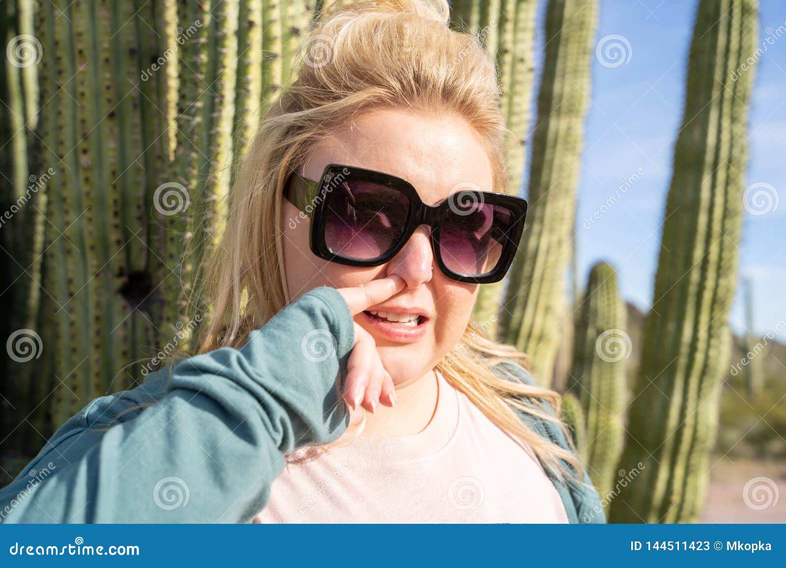 adult woman picks her nose in the desert, next to a giant organ pipe cactus in arizona