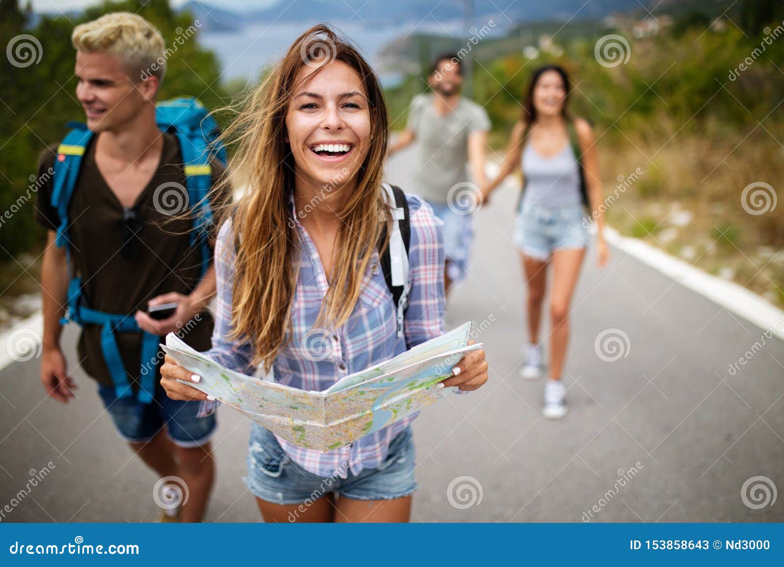 adventure, travel, tourism and people concept - group of smiling friends with backpacks and map