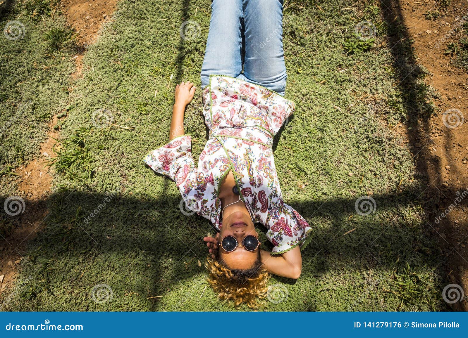 aerial point of view for pretty woman smile and rest laying down on a timo grass. hippy and fashion clothes with jeans. sunglasses