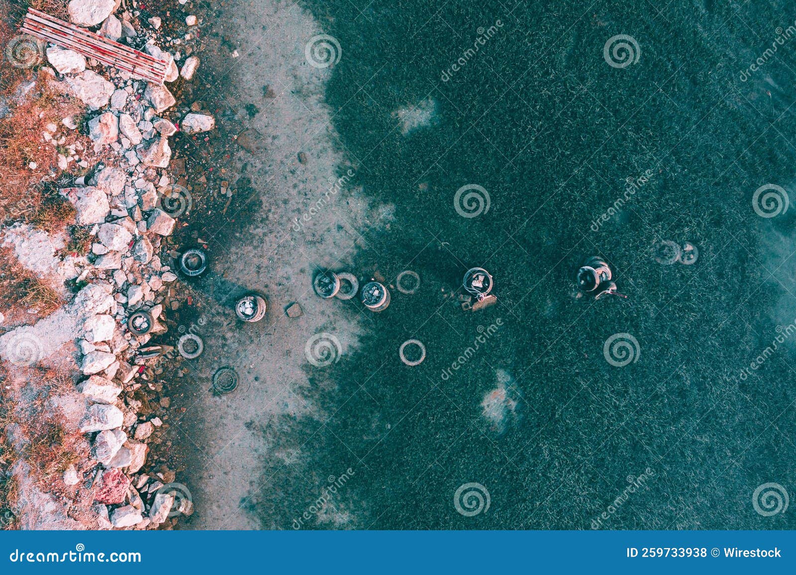 aerial top view of dirty trash tires and rocks on the shore of evoia, greece