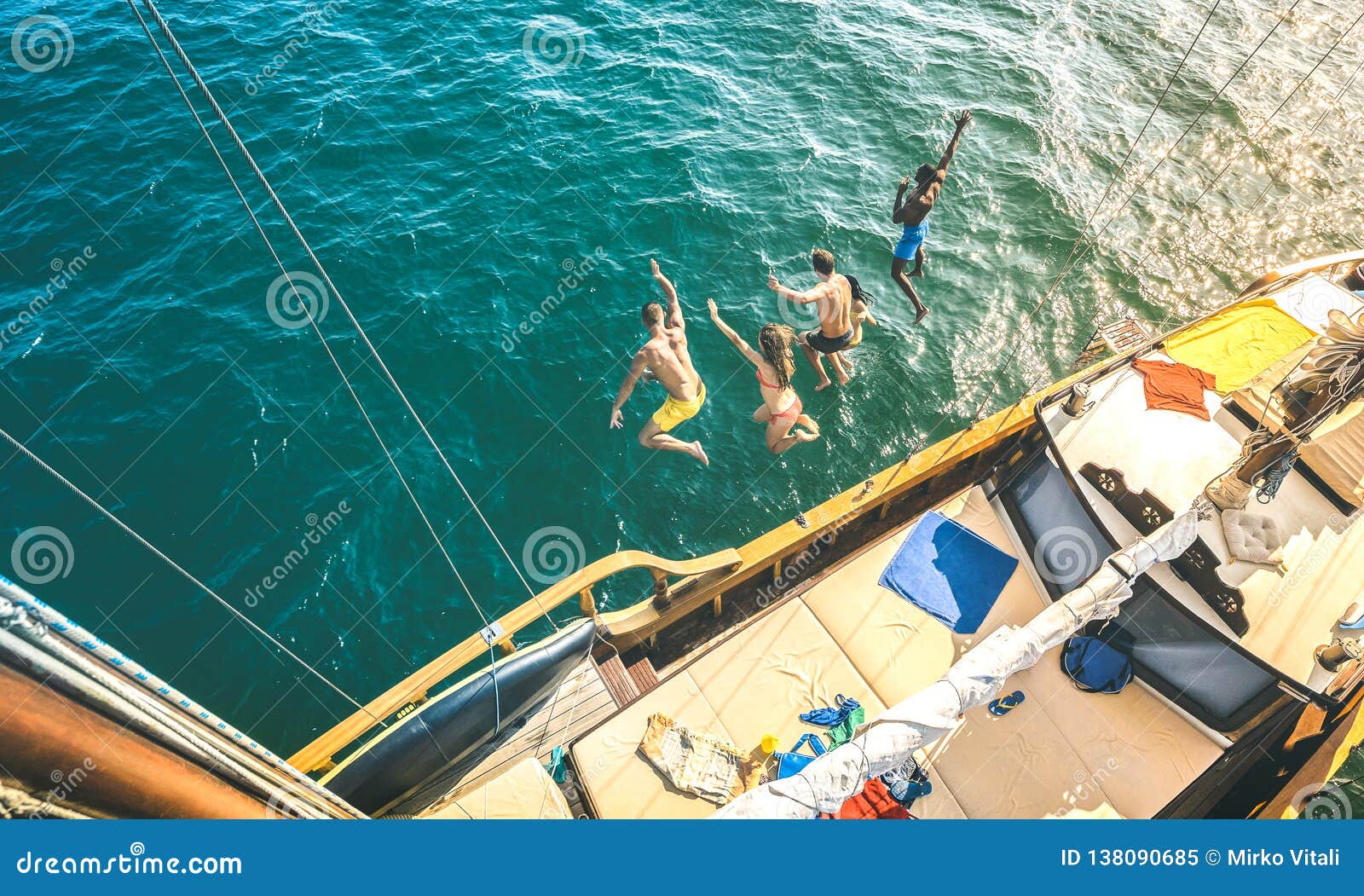 aerial view of happy millenial friends jumping from sailboat on sea ocean trip - rich guys and girls having fun together in