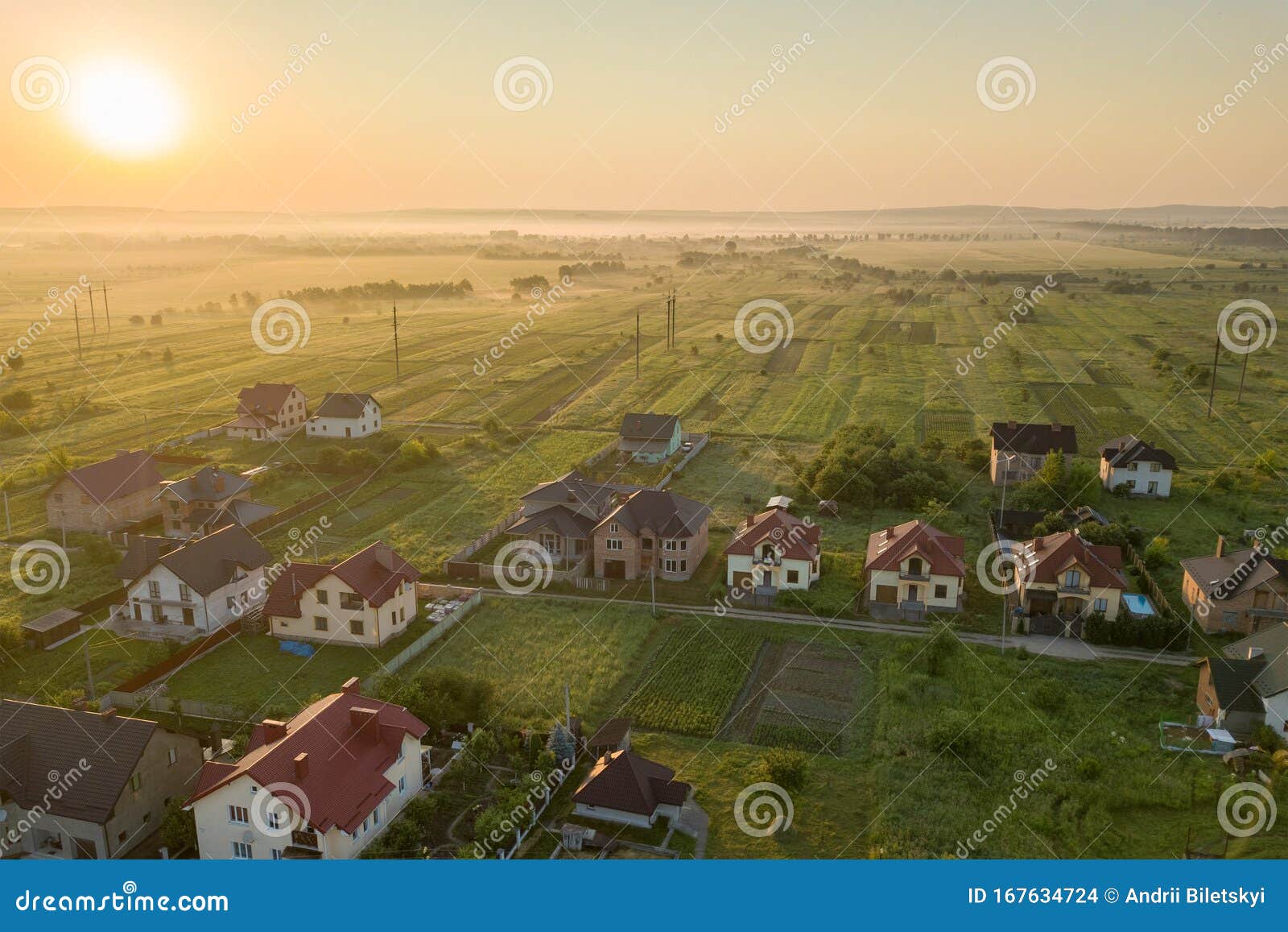 aerial view of rural residential area with private homes between green fields at sunrise