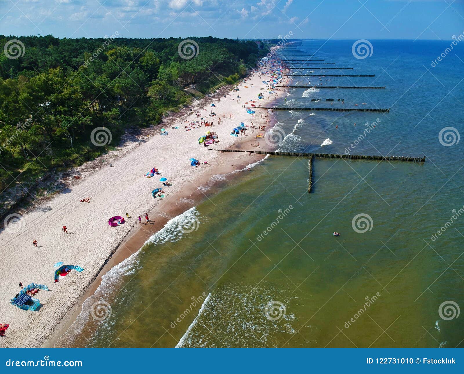 aerial view on sand beach, breakwaters, forest and sunbathers