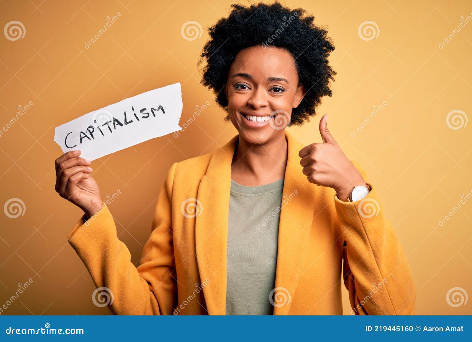african american afro businesswoman with curly hair holding paper with capitalism message happy with big smile doing ok sign,