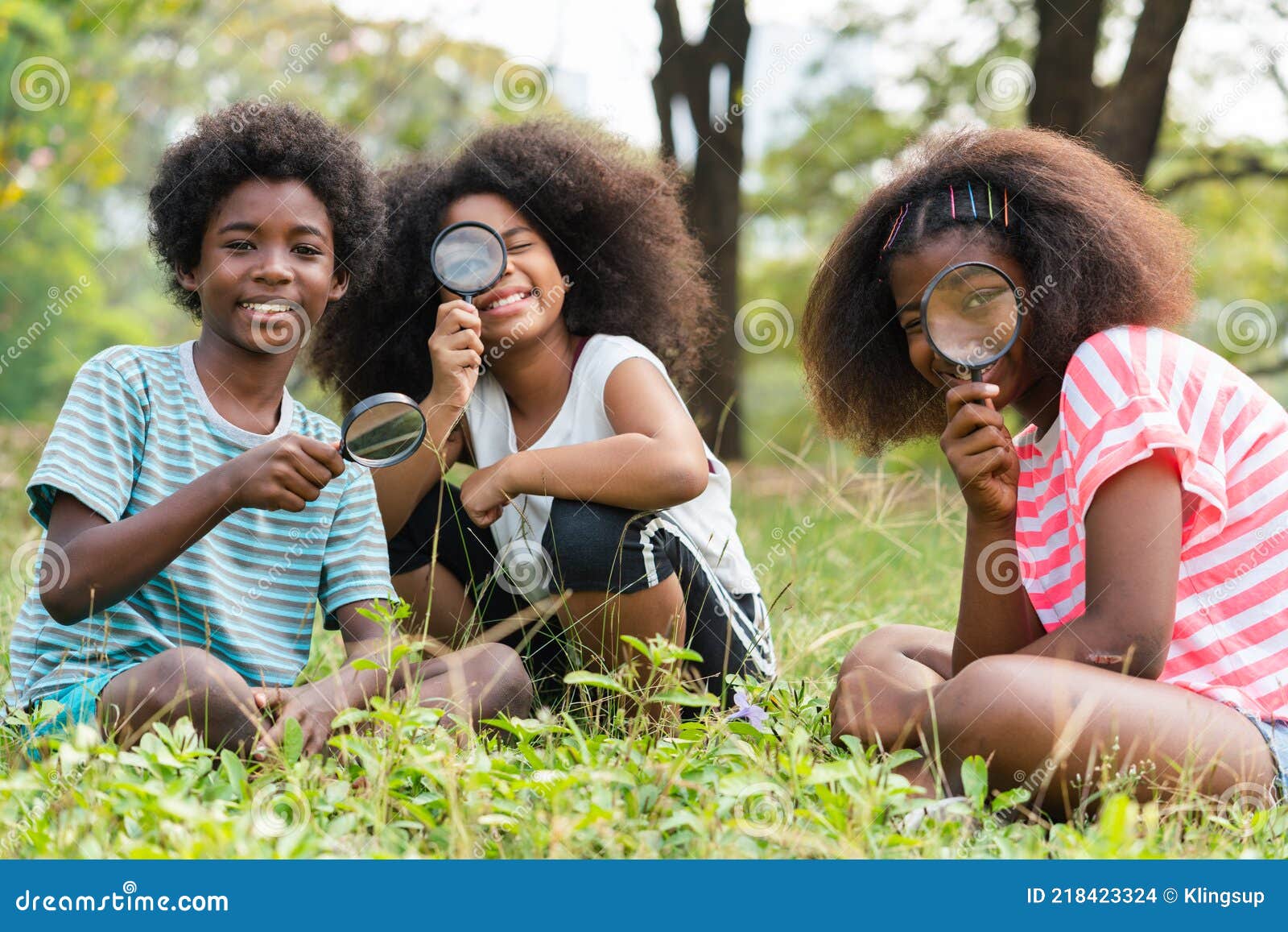 african american children sitting in the grass and looking through the magnifying glass between learn beyond the classroom. .