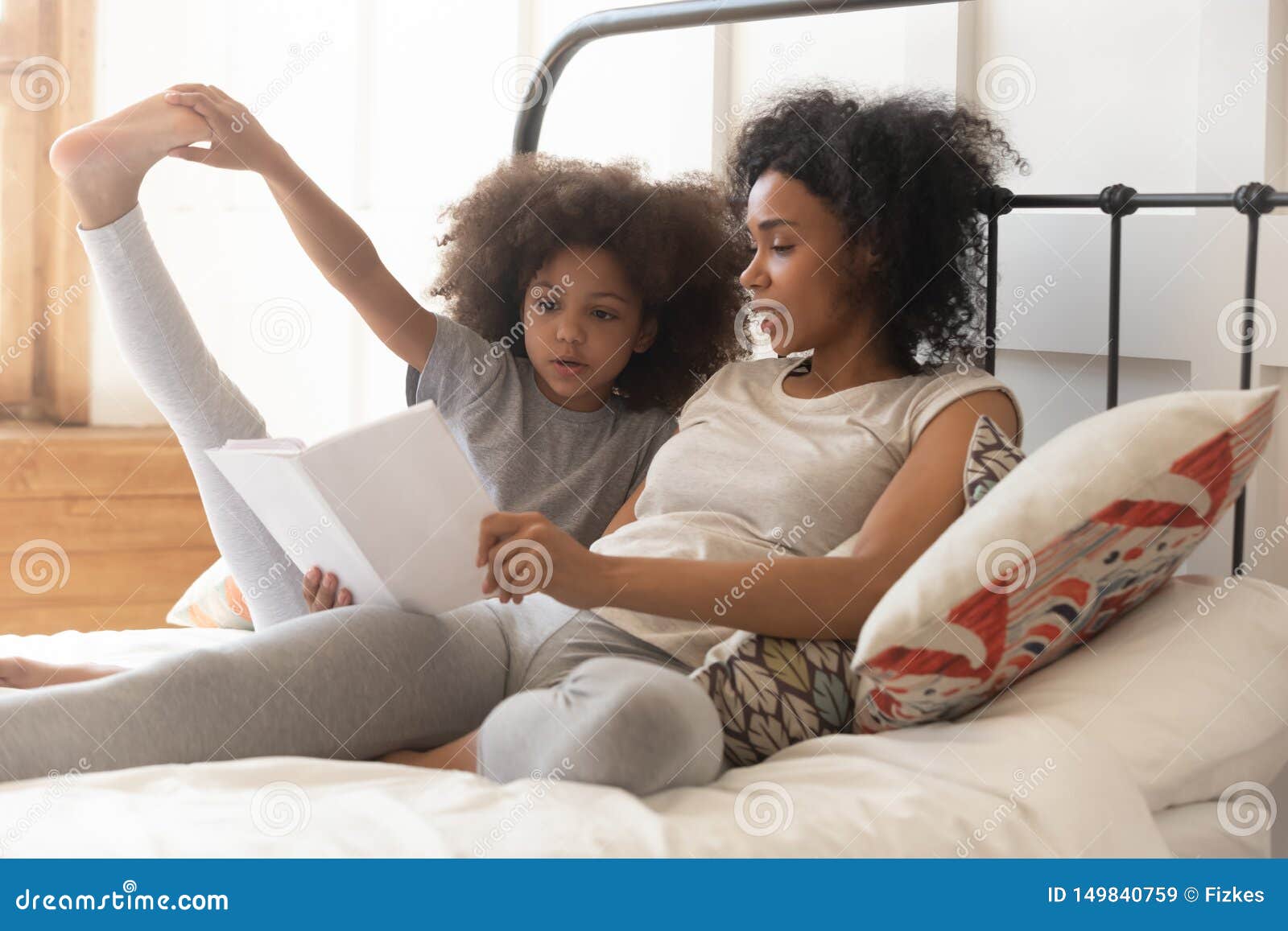 african mom and little kid daughter read book in bed