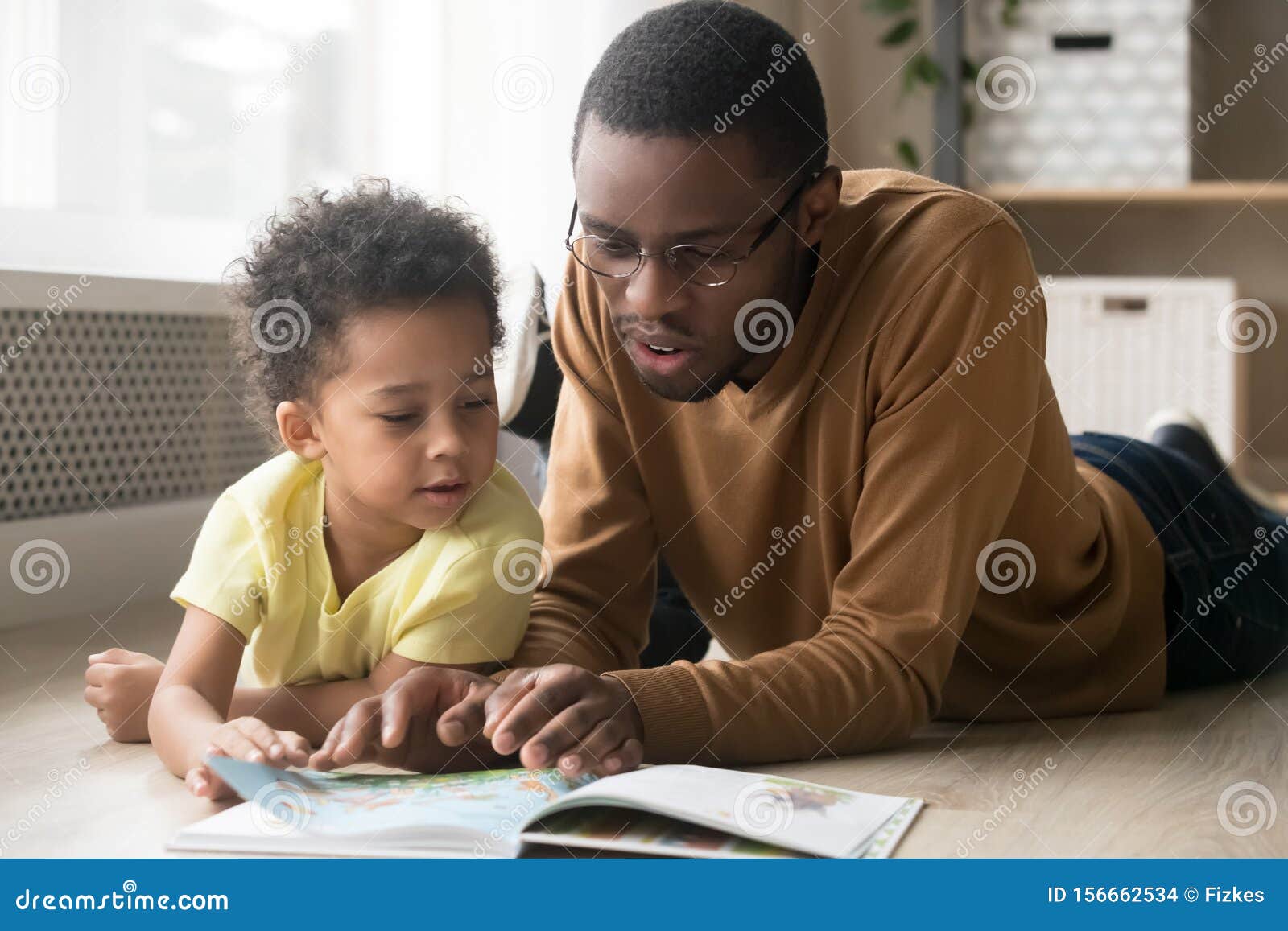 african american father and toddler son reading book together