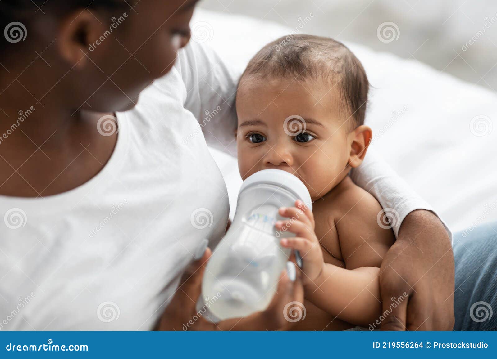 african american lady feeding her child from baby bottle