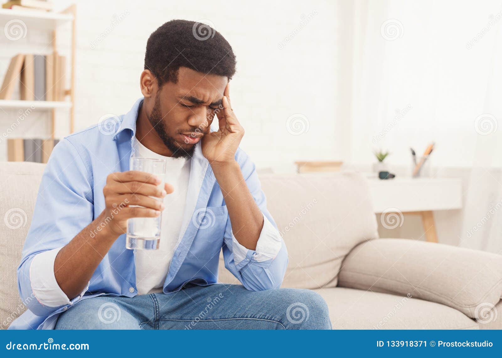 African-american man with headache taking pill at home. Exhausting headache. Sick african-american man taking pill with glass of water, suffering from migraine at home, copy space