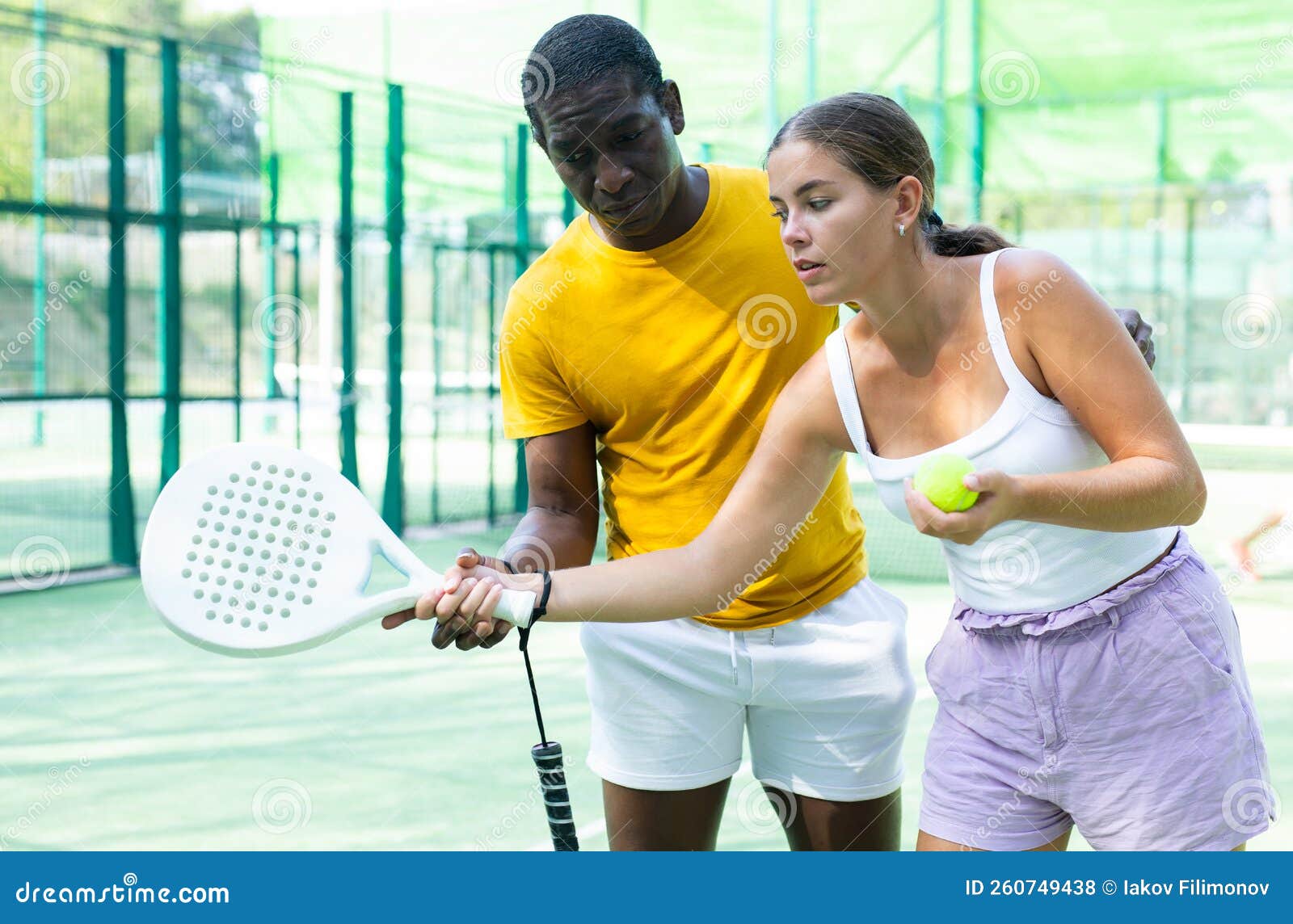 African American Man Instructor Teaches A Young Woman To Play Padel