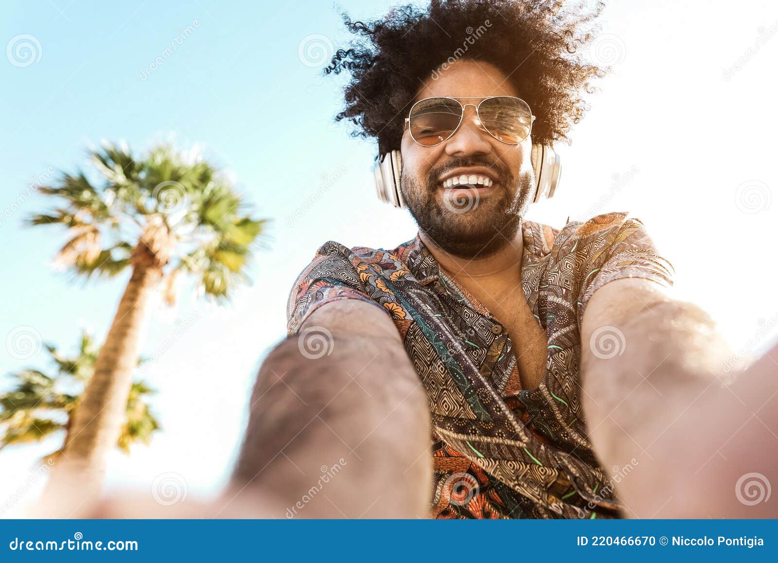 african american man listening music with headphones outdoor with palm trees in background - summer lifestyle, travel and party