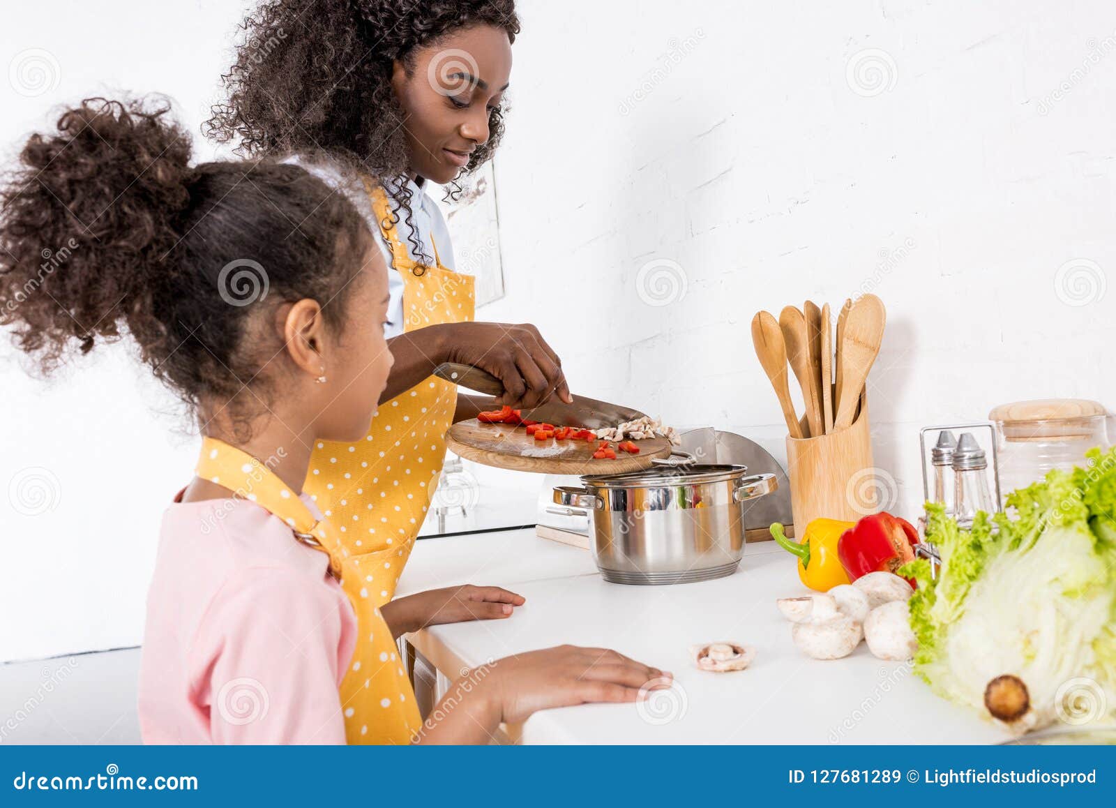 african american mother and daughter putting ingredientes in saucepan