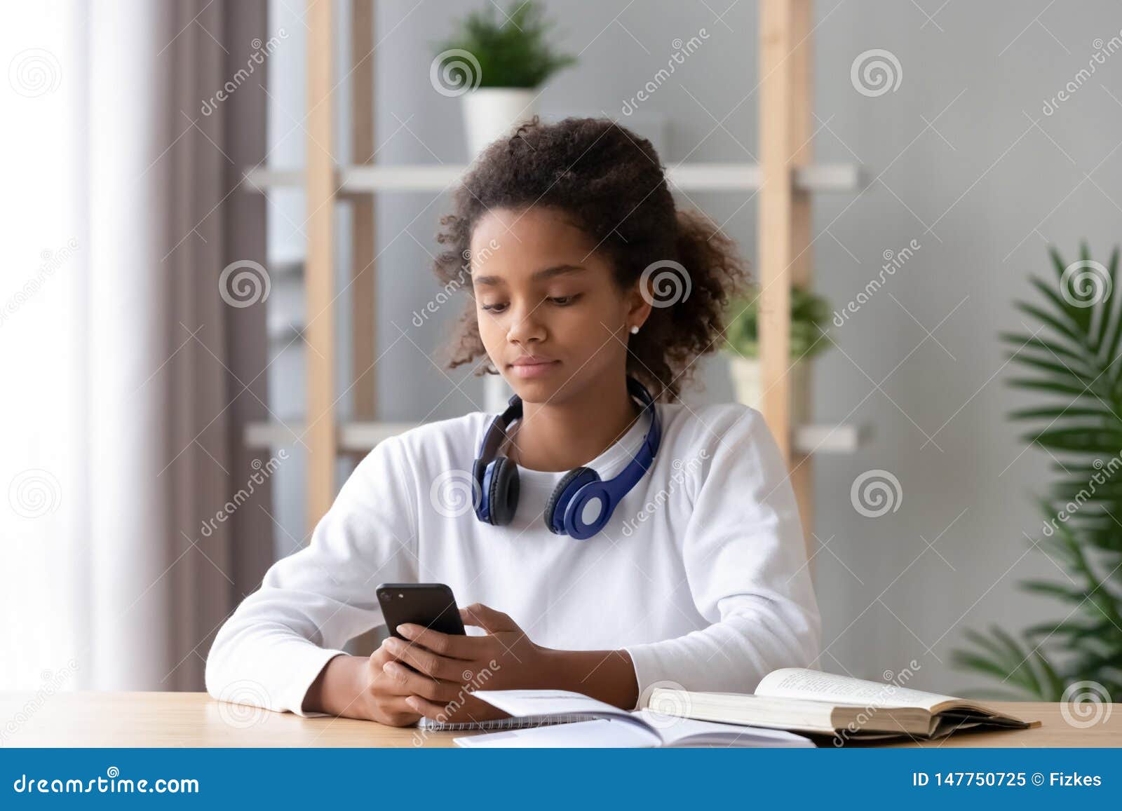 african american teen girl using phone, distracted from homework