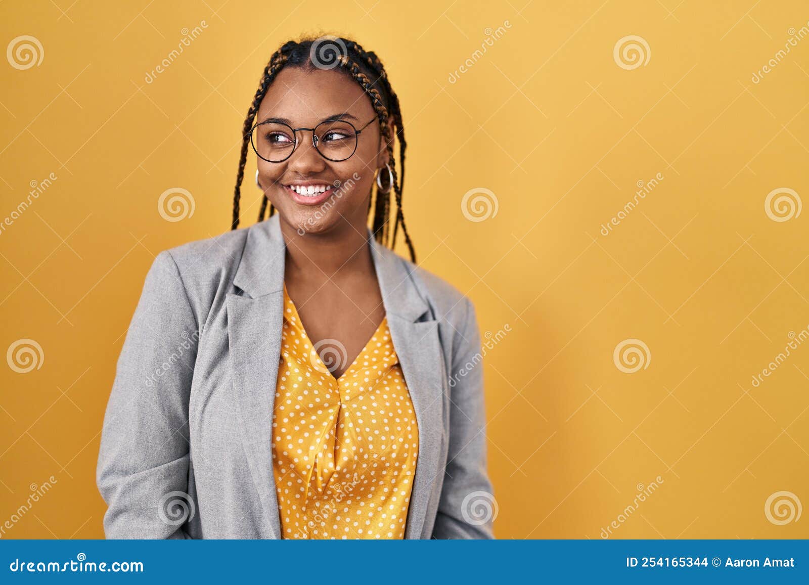 African american woman with braids standing over yellow background looking away to side with smile on face, natural expression. laughing confident