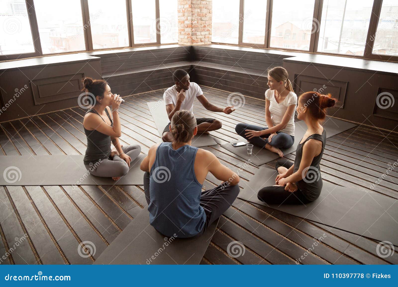 african-american yoga instructor talking to diverse group sittin