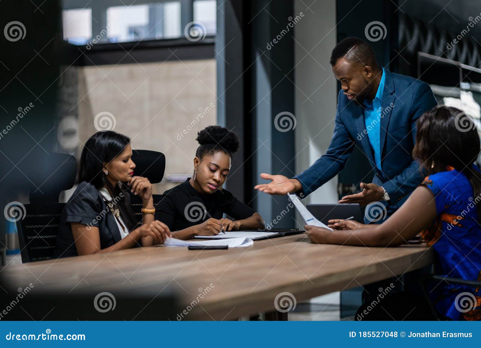 african businessman talking with a diverse group of female colleagues while having a meeting together around a table in an office