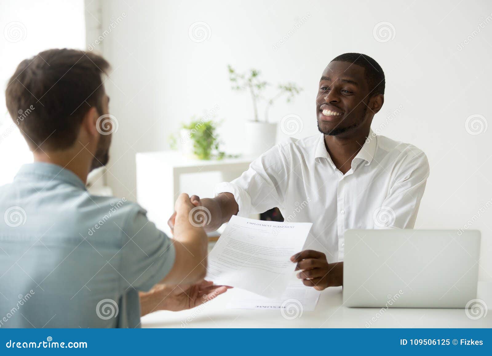 african employer handshaking new hire caucasian employee holding