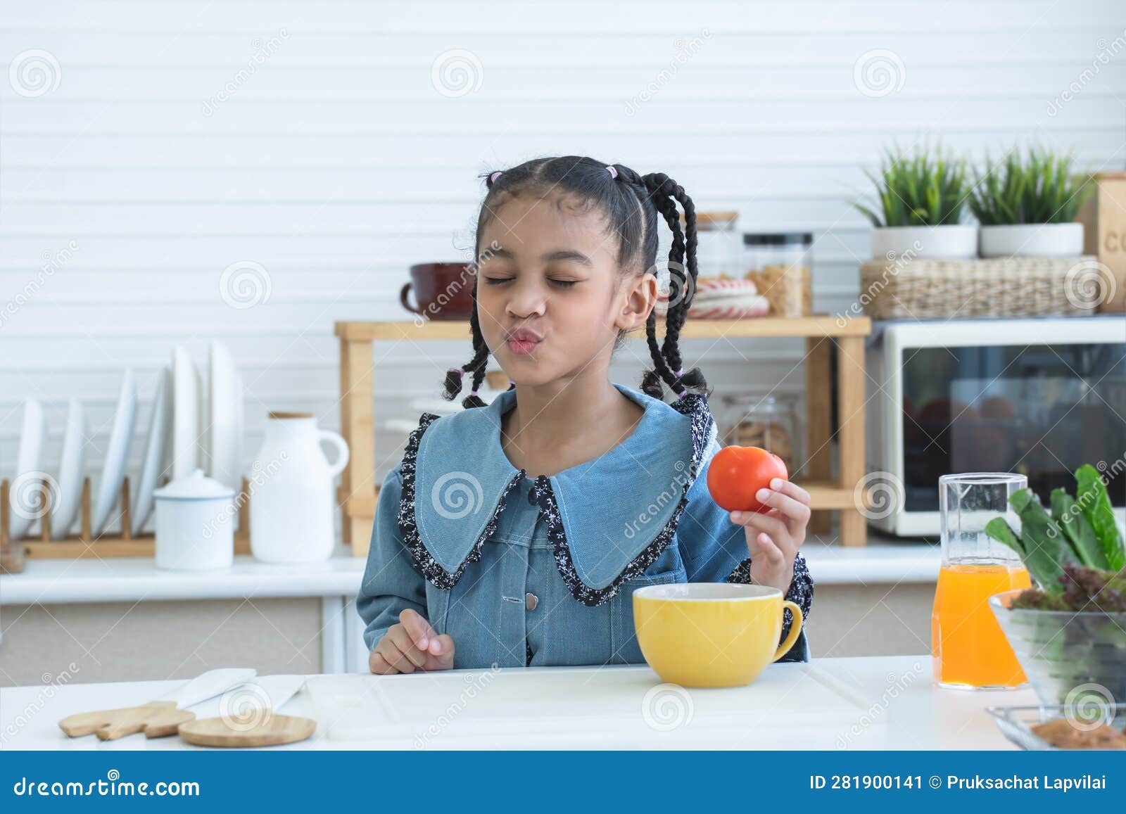 african little kid girl having fun with food and vegetables at kitchen, holding tomato, make a pucker lips, kissing. cute child