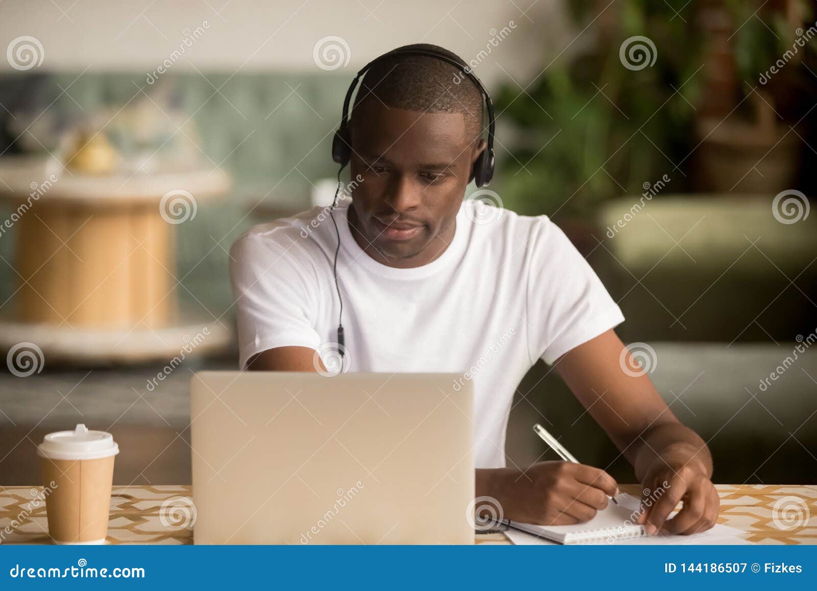 african man wearing headphones watching webinar making notes study online