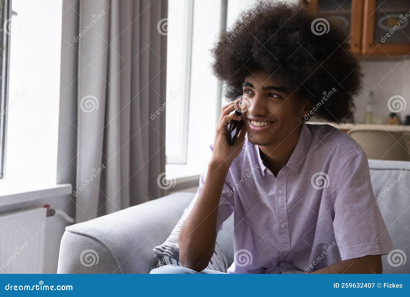 african teenage guy sits on sofa blab on cell phone