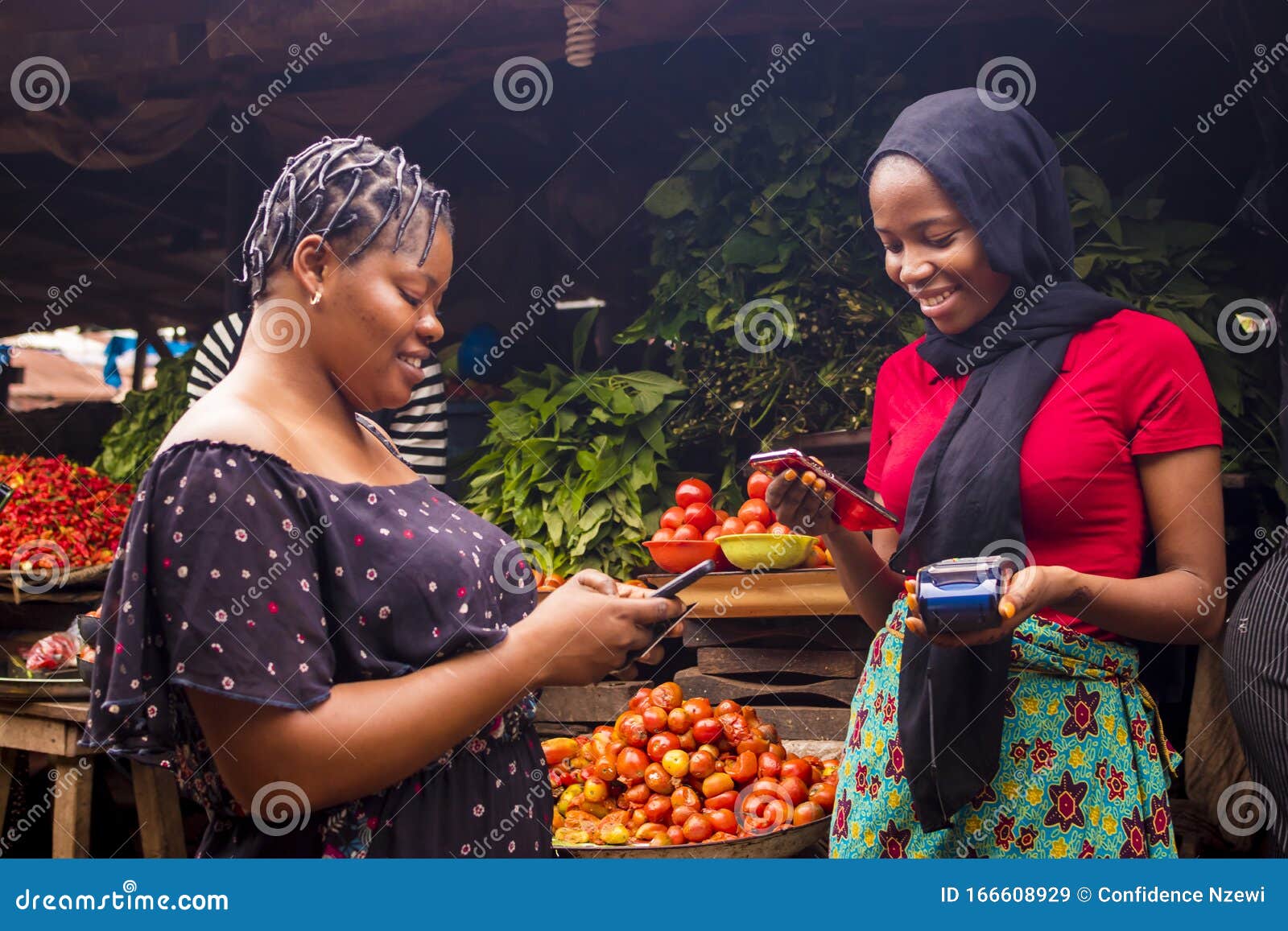 african woman shopping food stuff in a local market paying by doing mobile transfer via phone for a trader
