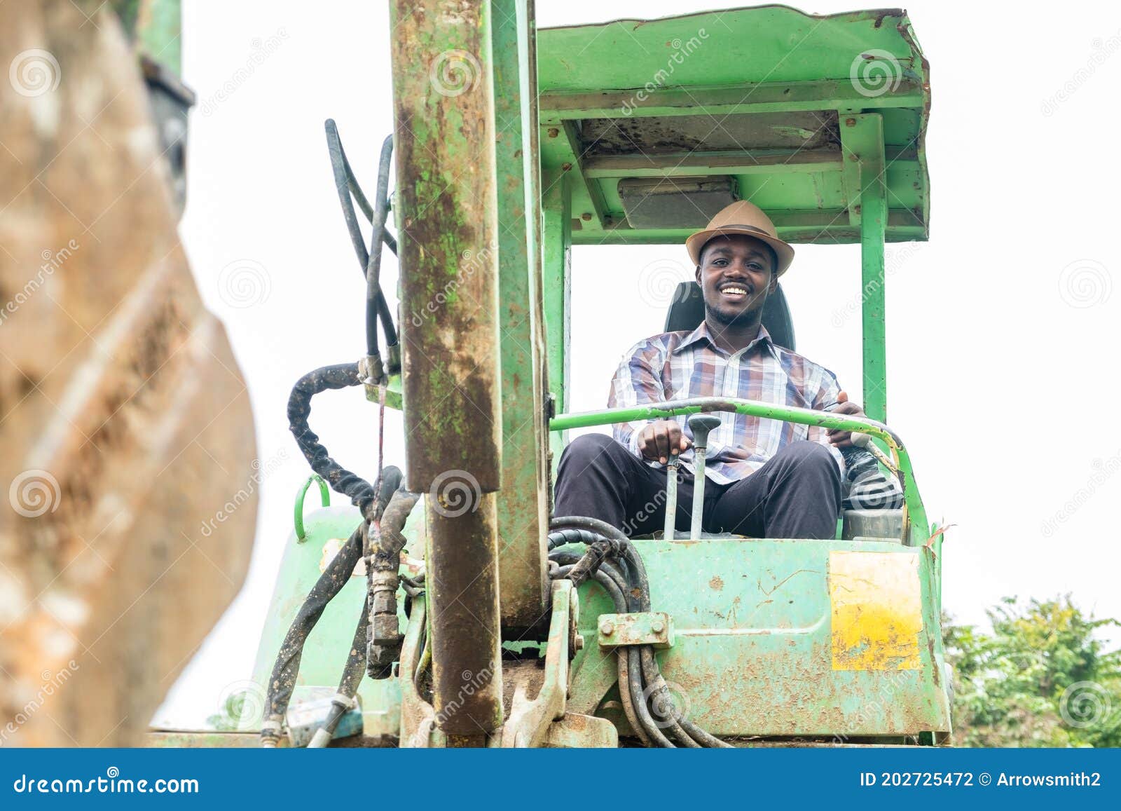 African Worker Driving Heavy Construction Equipment Backhoe with Smile and Happy Stock Photo