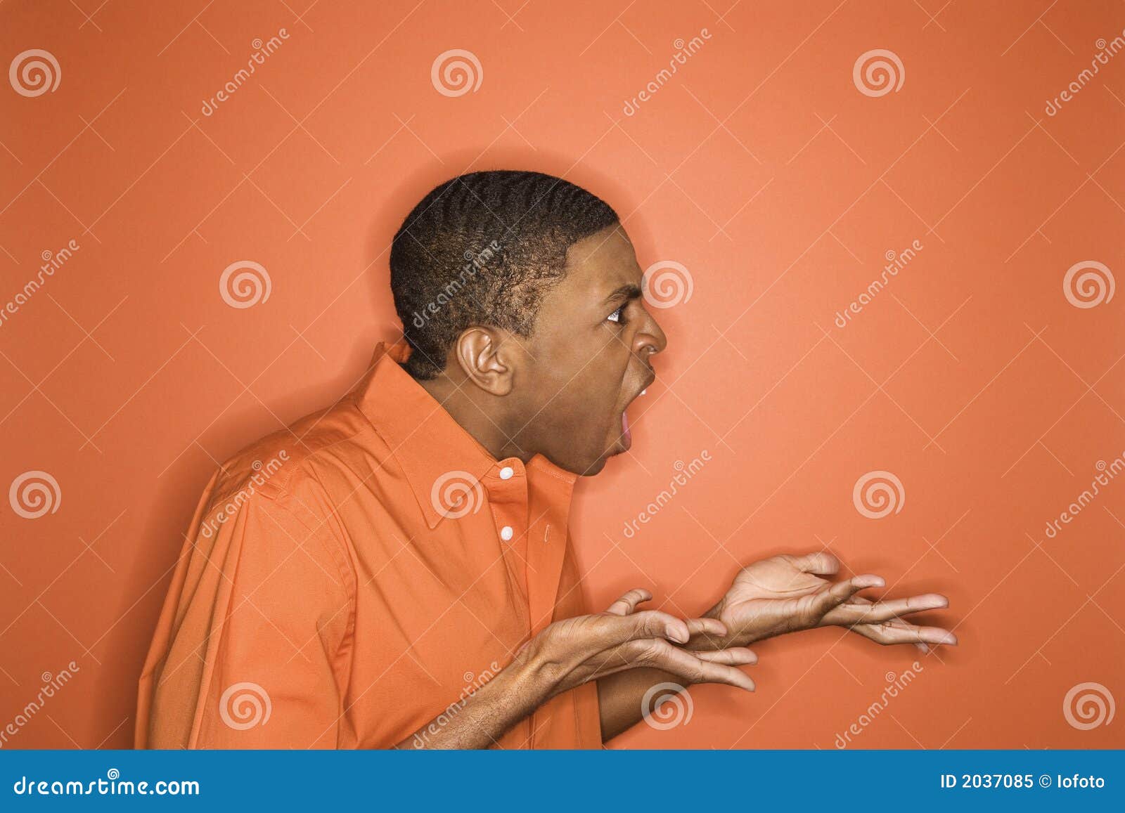 Afrikaans-Amerikaanse mens die woede uitdrukt. Zijaanzicht van de jonge Afrikaans-Amerikaanse mens die op oranje achtergrond woede naar unseen persoon uitdrukt.