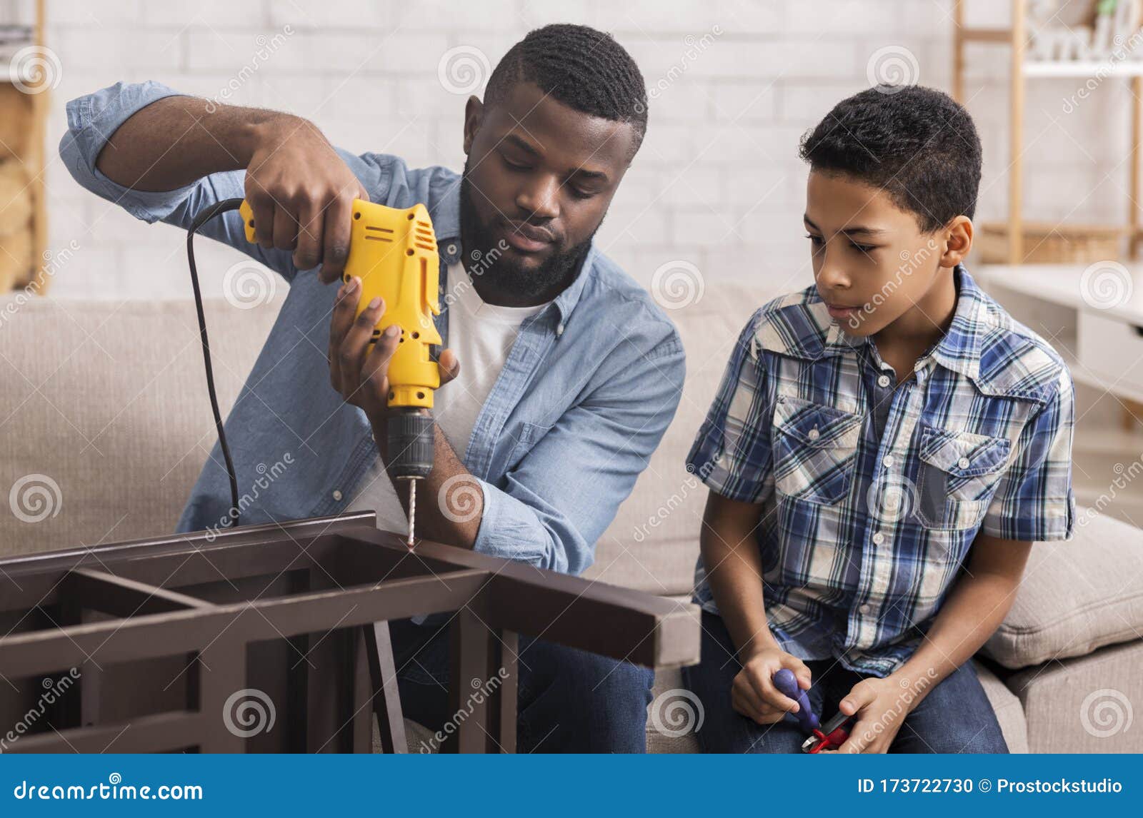 afro dad teaching preschool son to use electric drill at home