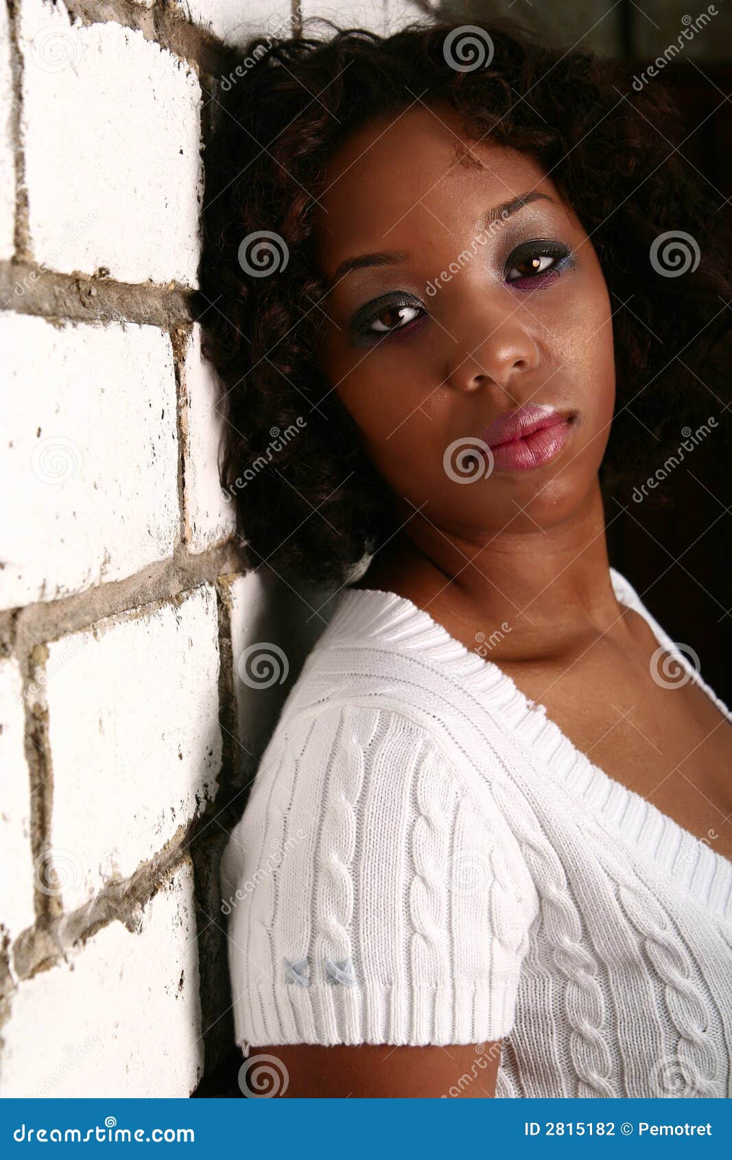 Afroamerikaner-Mädchen-Mageres ein. Afroamerikanermädchen mit dem unschuldigen Blick, der den unbelegten Ausdruck lehnt sie zurück zu weißer Backsteinmauer zeigt