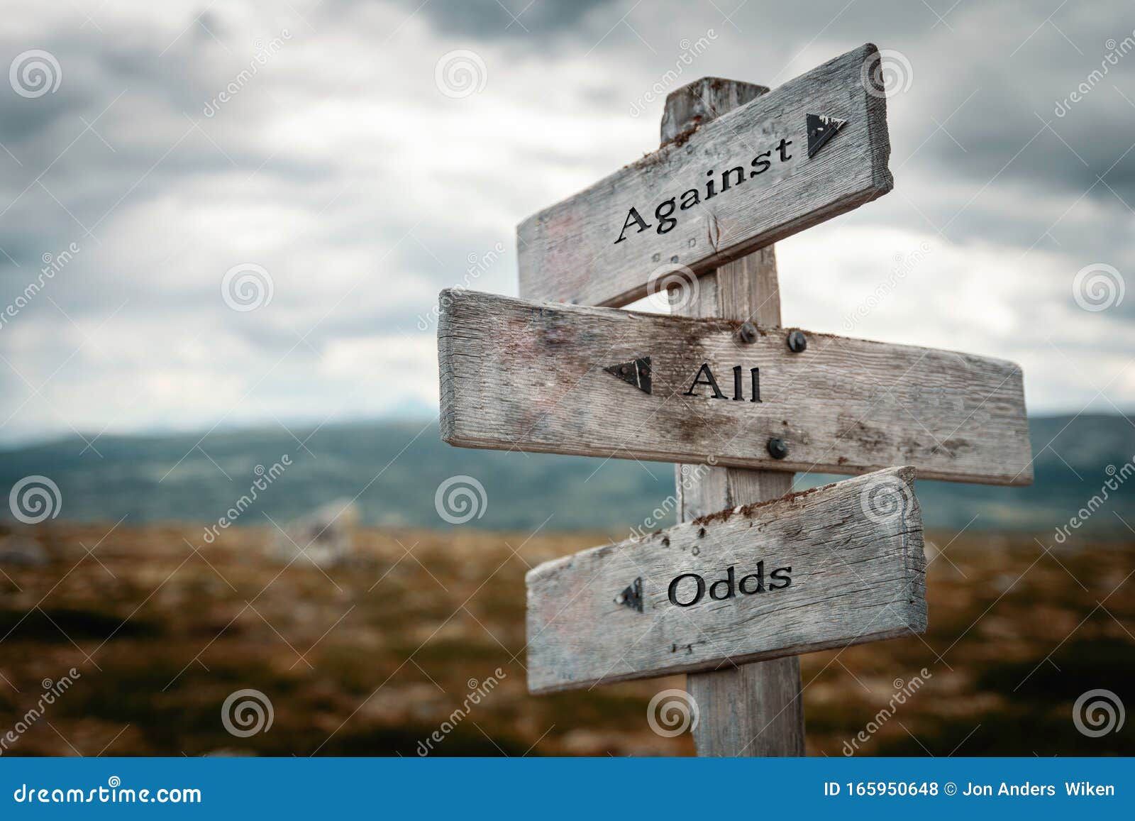 against all odds text on wooden rustic signpost outdoors in nature/mountain scenery.
