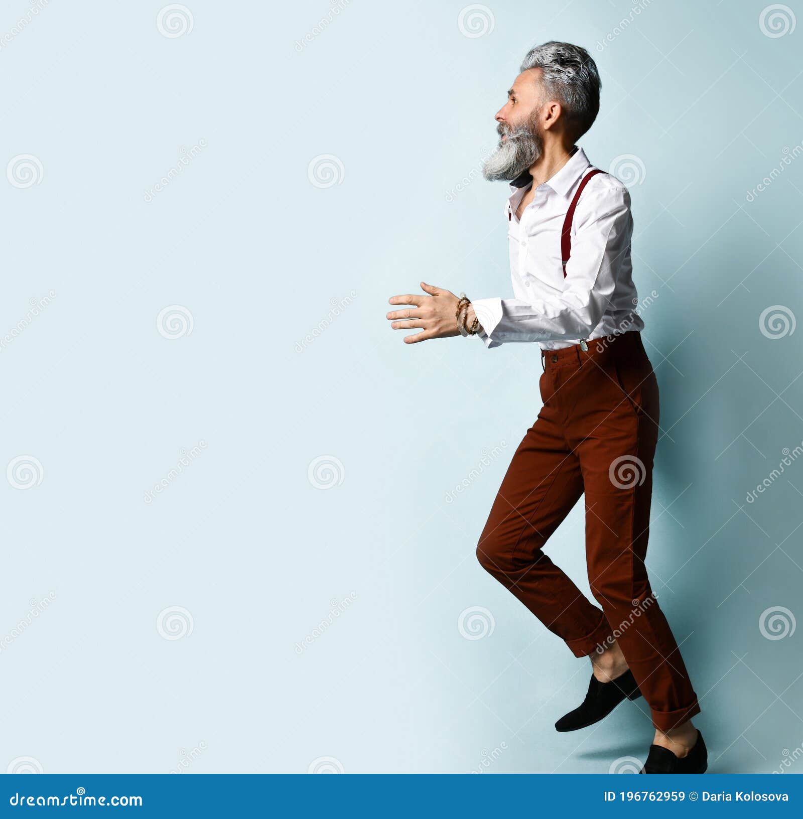 Gray-haired, Bearded Male In White Shirt, Brown Pants And Suspenders, Black  Loafers. He Runs Looking Back, Posing Sideways Against Blue Studio  Background. Fashion And Style. Full Length, Copy Space Stock Photo, Picture