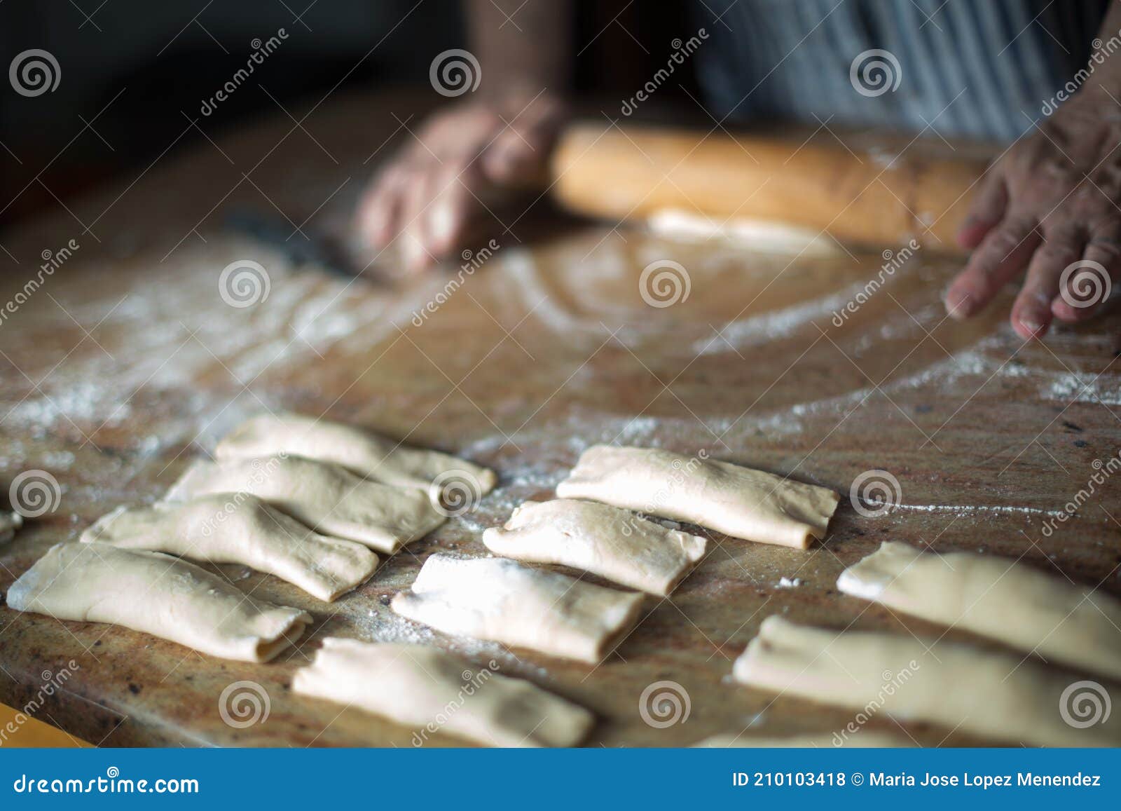 aged woman`s hands with a rolling pin preparing at home casadielles filled with nuts. tradicional gastronomy