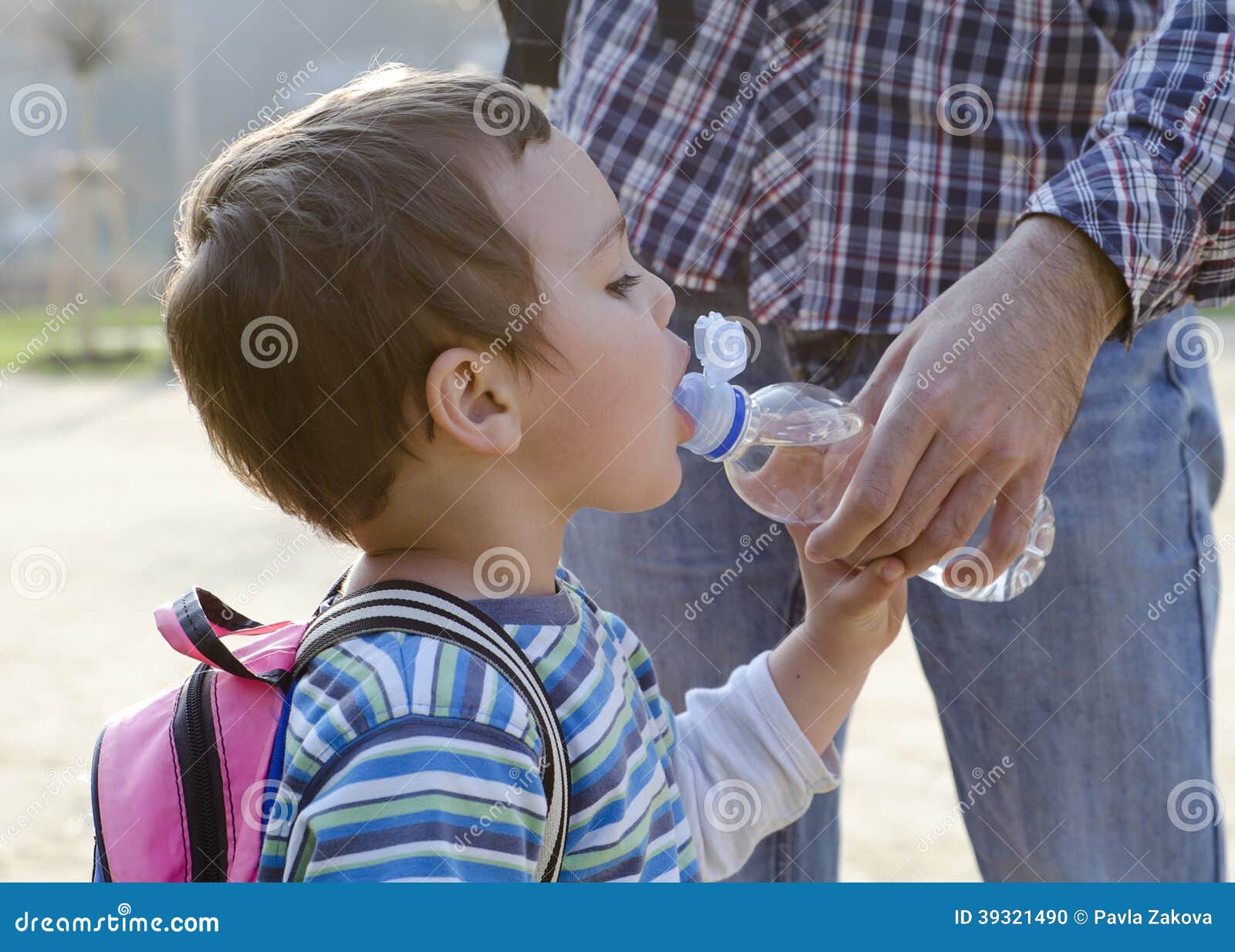 Agua potable del niño de una botella platic, su padre que le ayuda.