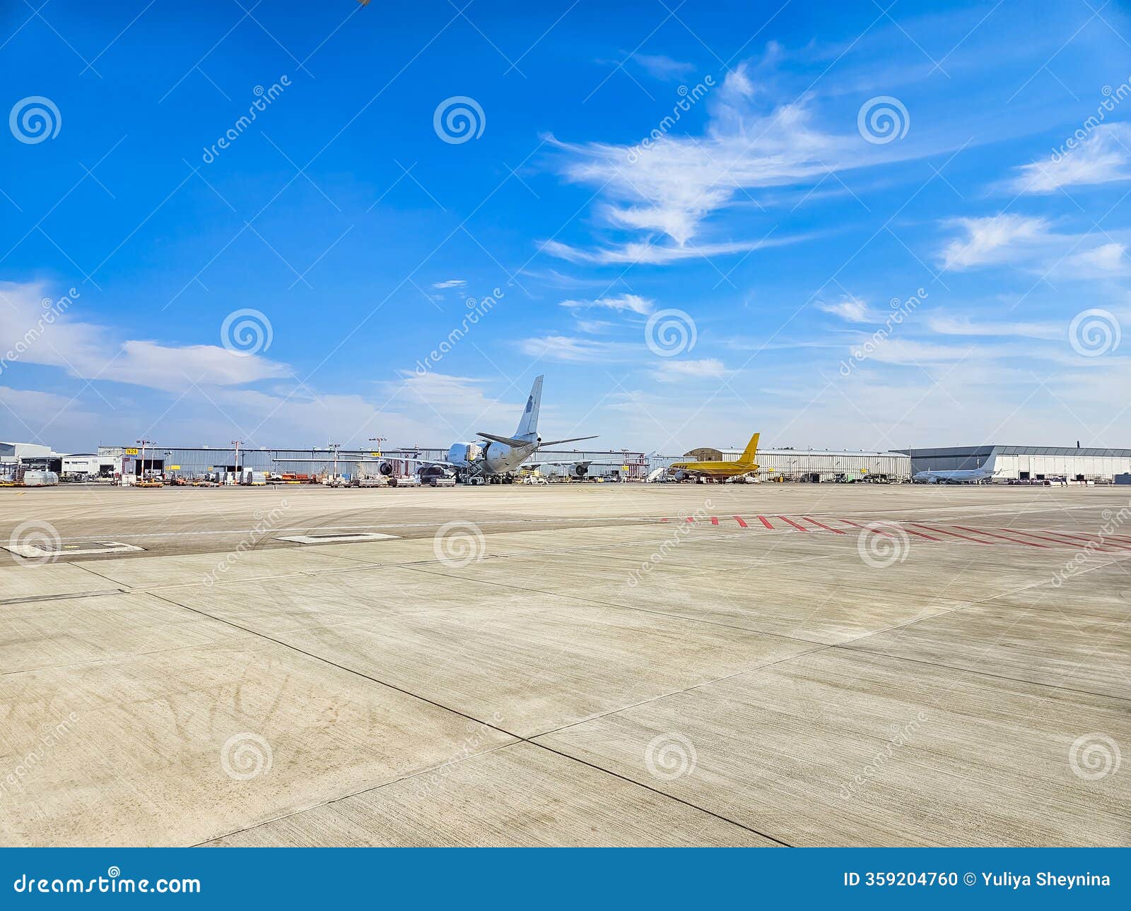airport tarmac with parked planes under a blue sky with scattered clouds