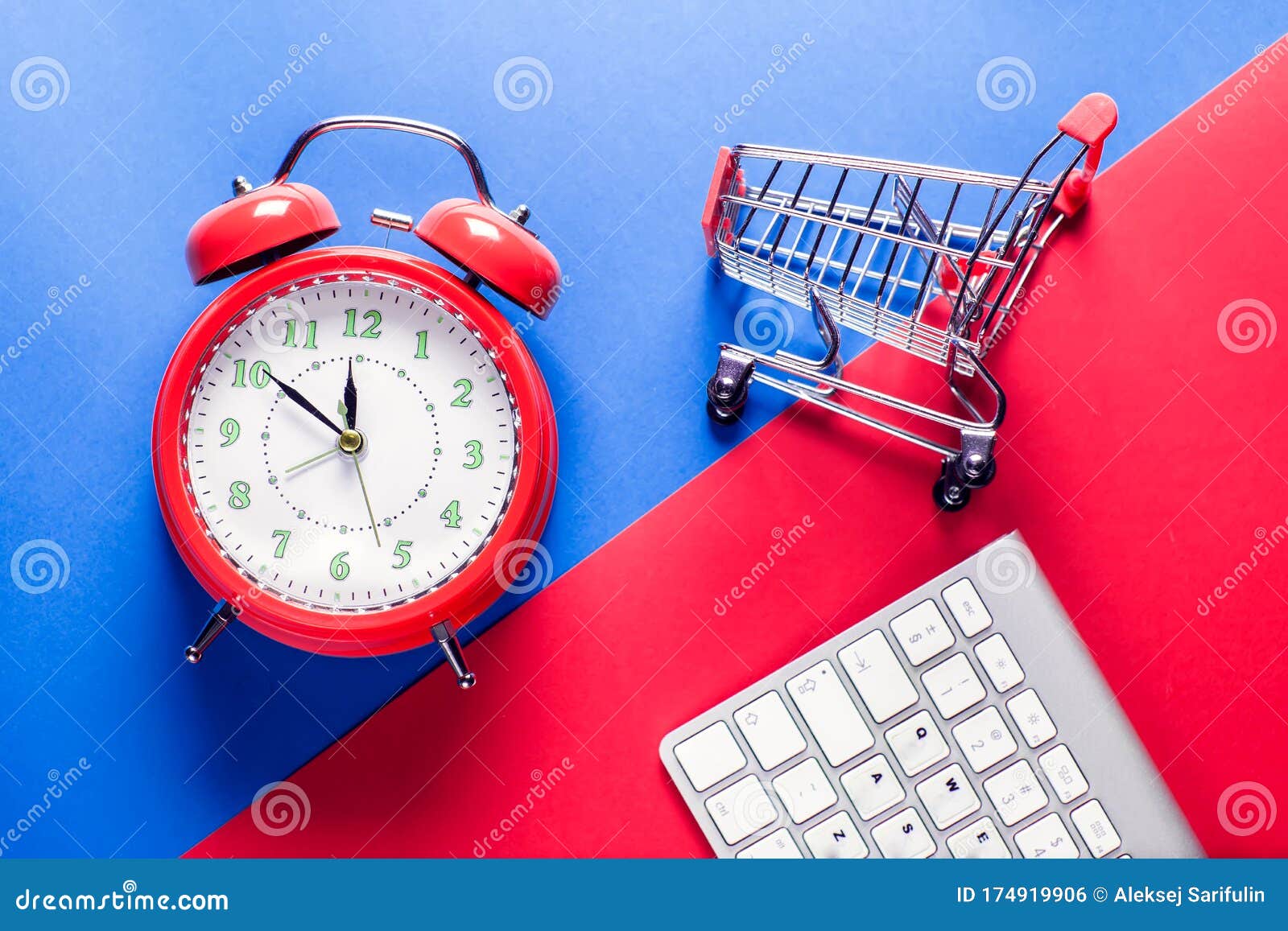 alarm clock, shopping trolley and keyboard on the doubble color background. online shopping and sales concept