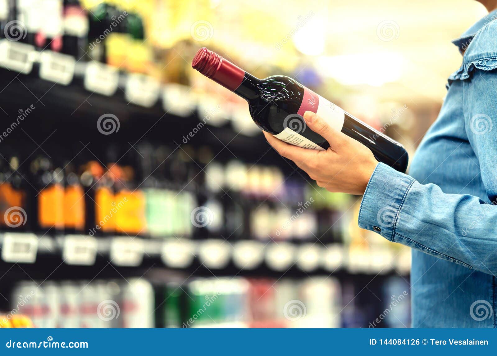 alcohol shelf in liquor store or supermarket. woman buying a bottle of red wine and looking at alcoholic drinks in shop.