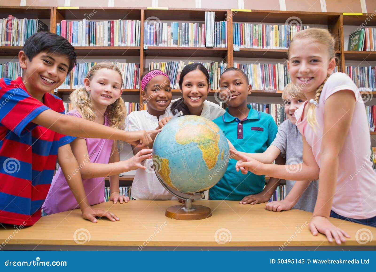 Allievi svegli ed insegnante che esaminano globo in biblioteca la scuola elementare