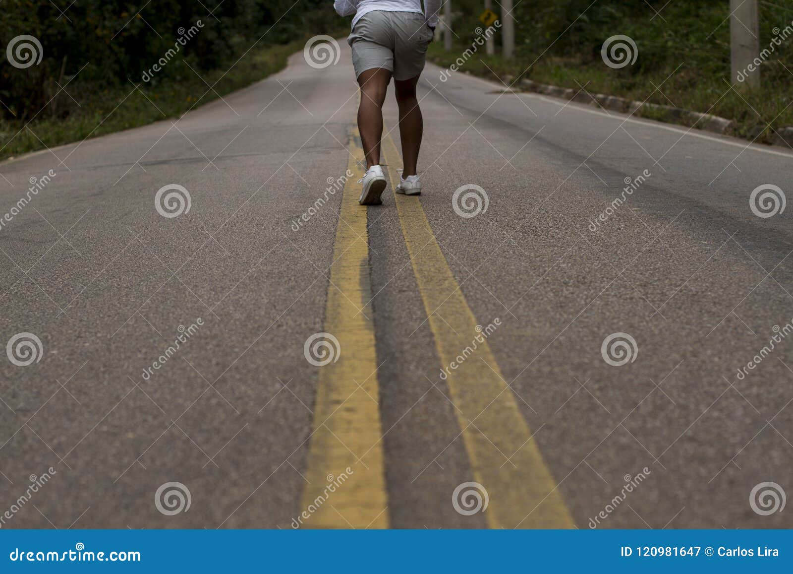 Allungamento delle gambe per pareggiare di mattina. L'uomo esegue solo sulla strada calma in mezzo alla foresta, all'esercizio fisico ed alla buona forma