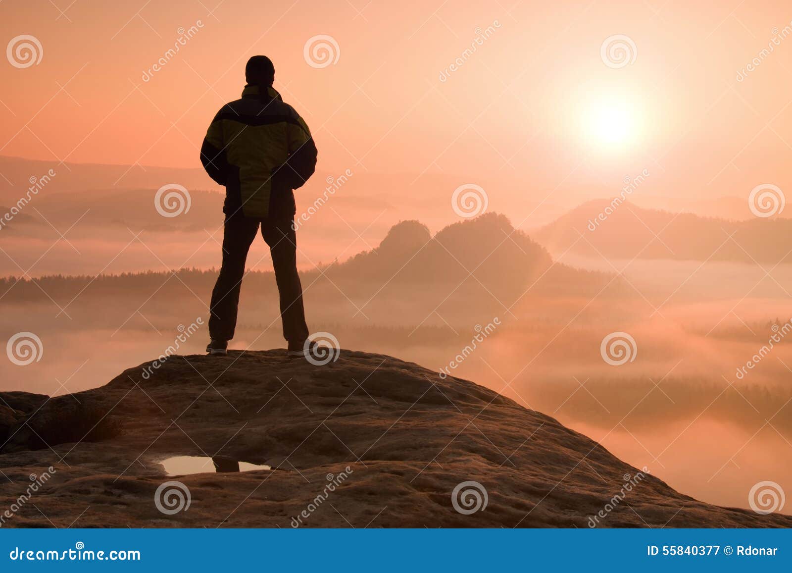 alone hiker standing on top of a mountain and enjoying sunrise