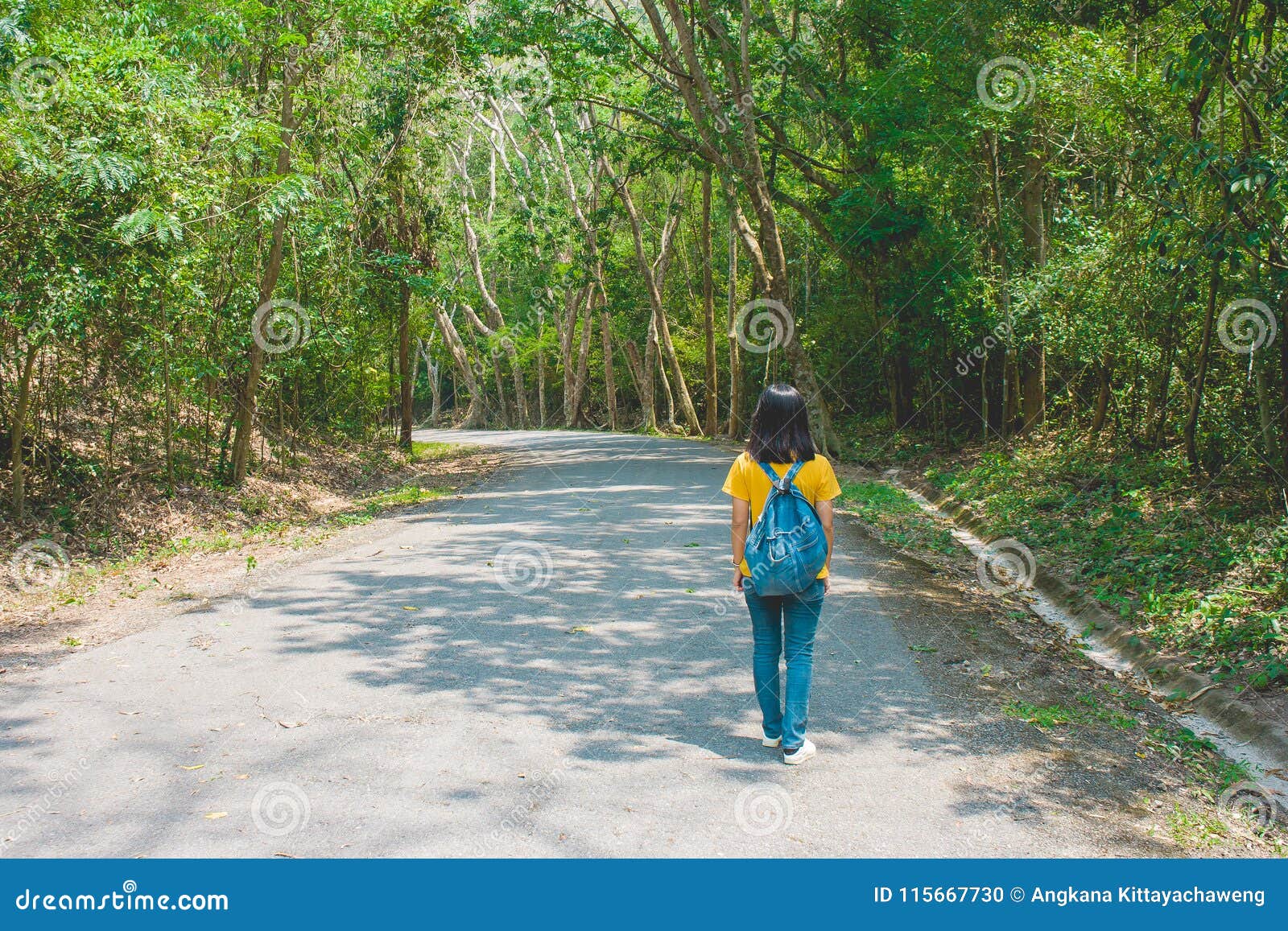 alone woman traveller or backpacker walking along contryside road among green trees.