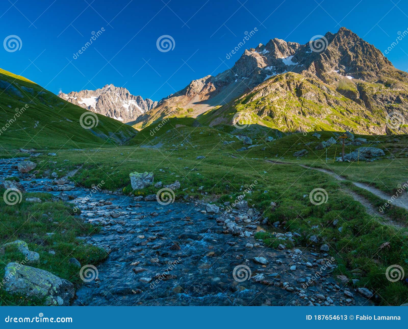 Alpine Stream In Idyllic Valley Amid Rocks And Green Meadows Natural