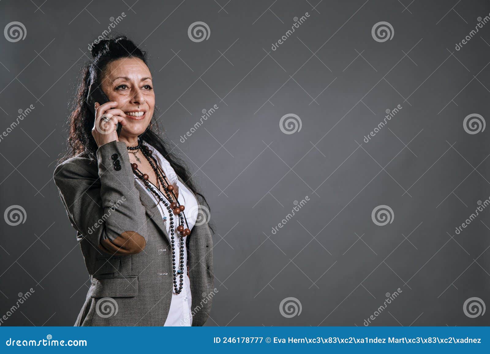 alternative woman dressed in jacket suit smilingly attends to her mobile phone in study shot