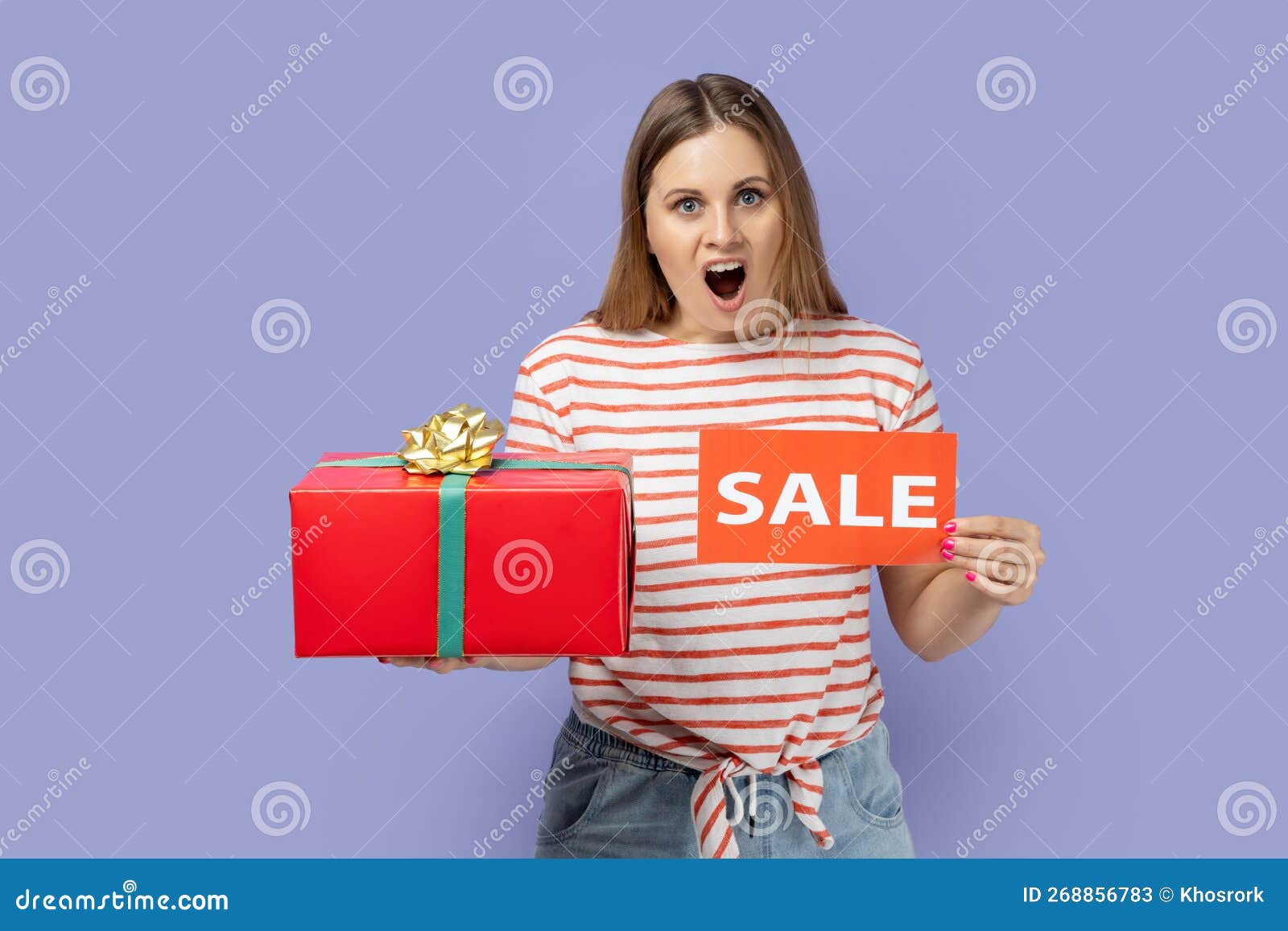 amazed shocked woman standing with sale card and red gift box in hands, big bonus for holiday.