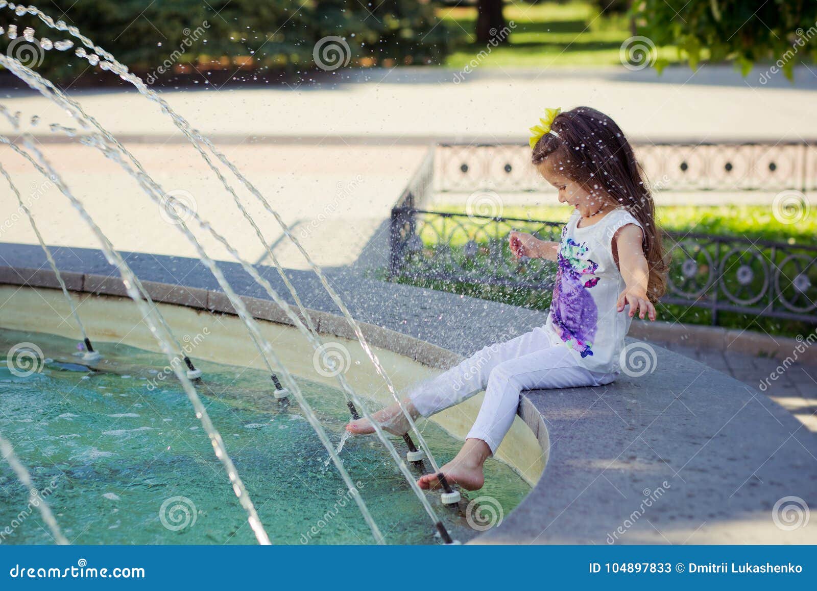 amazing scene of little fashion baby child girl playing summer time with fountain by ner tiny barefoot legs wearing fancy clothes