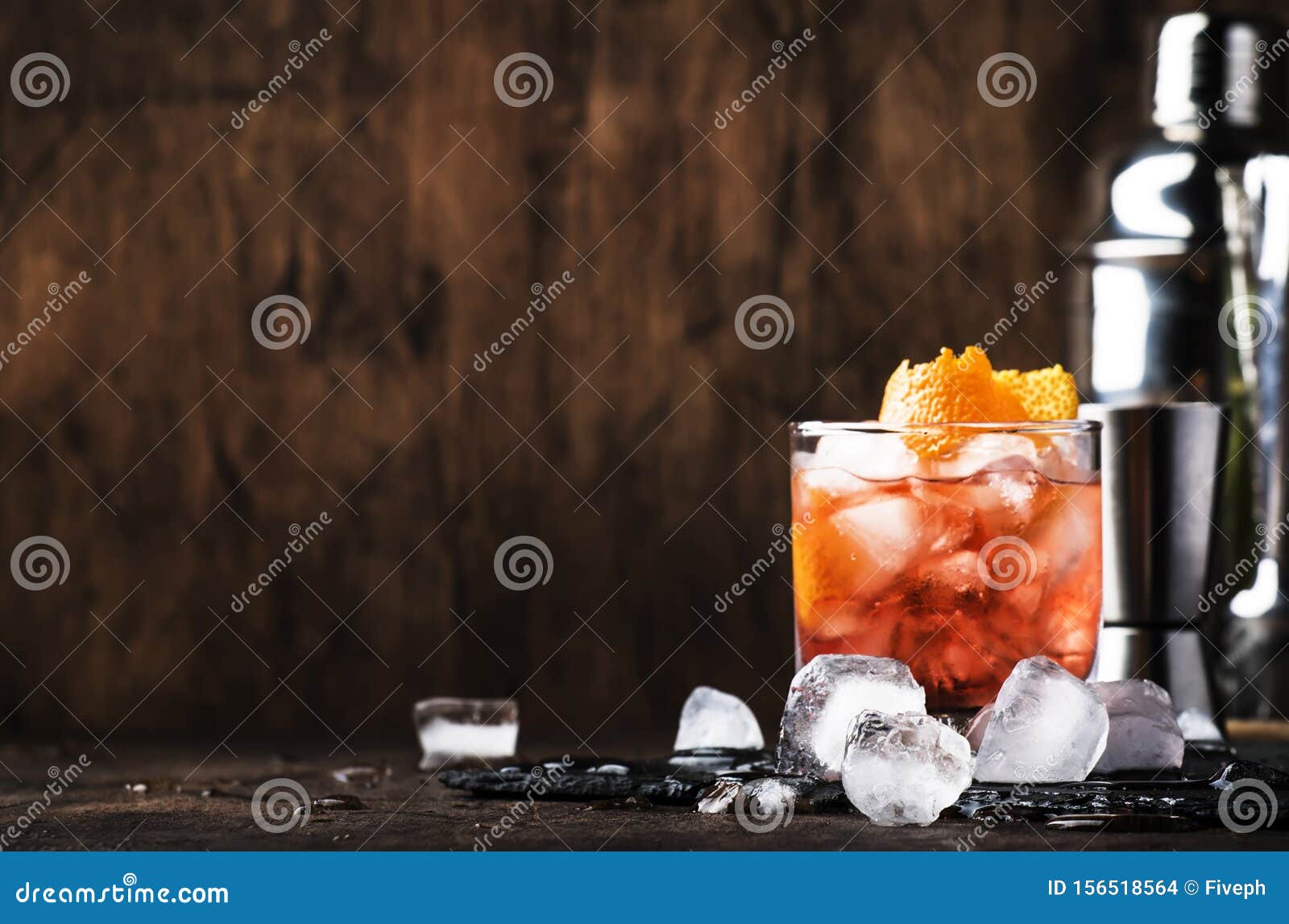 americano alcohol cocktail with red vermouth, bitter, soda, orange zest and ice, dark wooden bar counter background, bar tools,