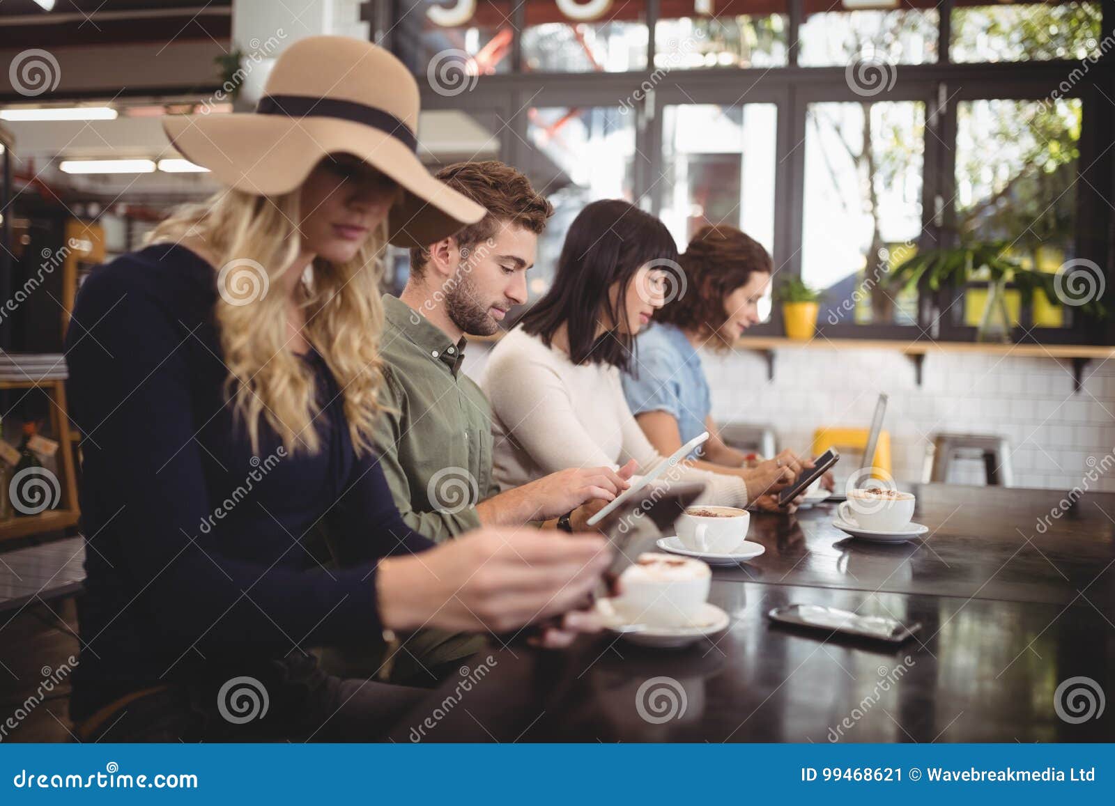 Amici che utilizzano i telefoni cellulari mentre sedendosi con le tazze di caffè nel caffè. Giovani amici che utilizzano i telefoni cellulari mentre sedendosi con le tazze di caffè alla tavola nel caffè